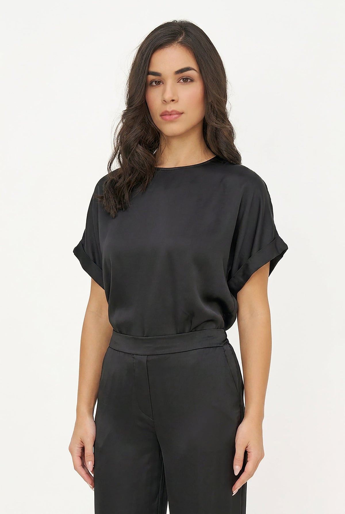 A woman modeling a black short-sleeve top with a matching black belt and trousers, photographed against a clean white studio background.