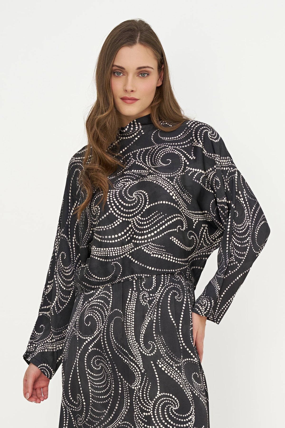 A woman modeling a black long-sleeve dress with a white swirling dot pattern, set against a plain light gray studio background.