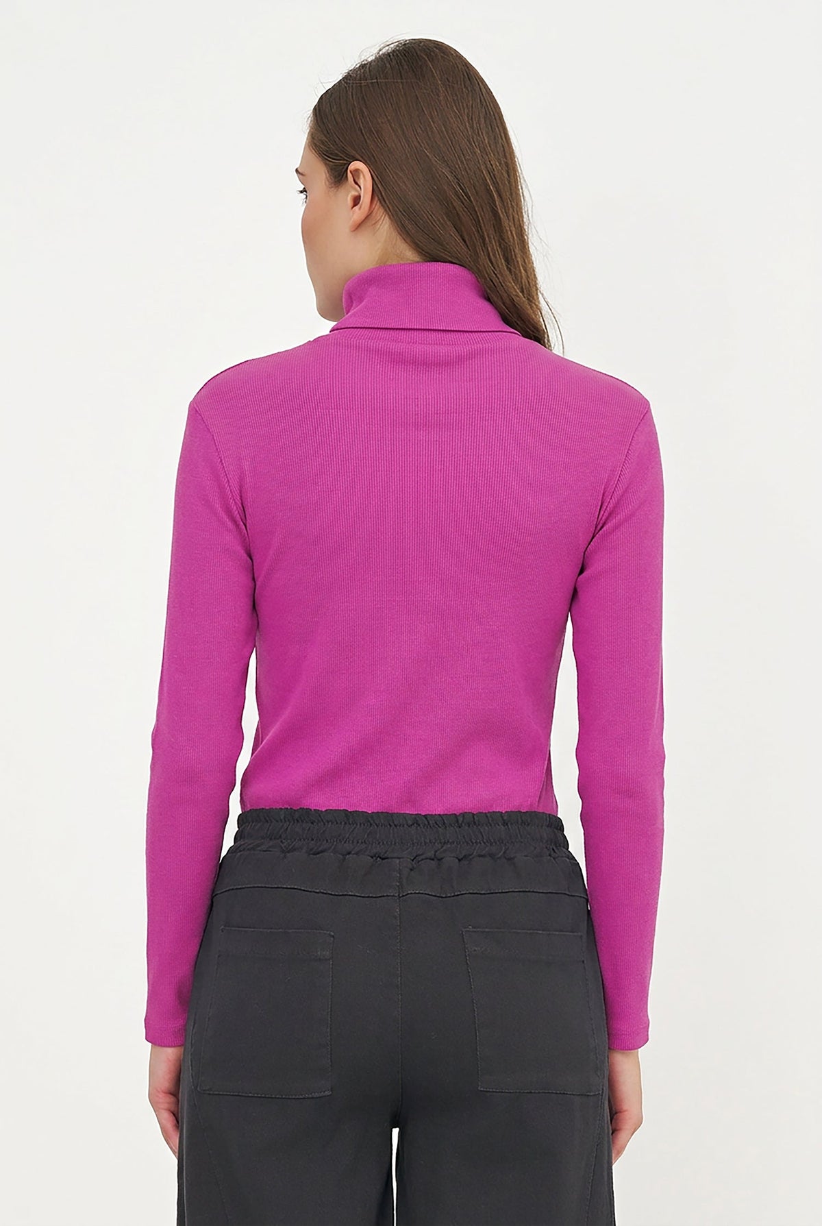 A woman viewed from the back wearing a bright magenta long-sleeve mock neck top and dark gray pants against a plain white background.