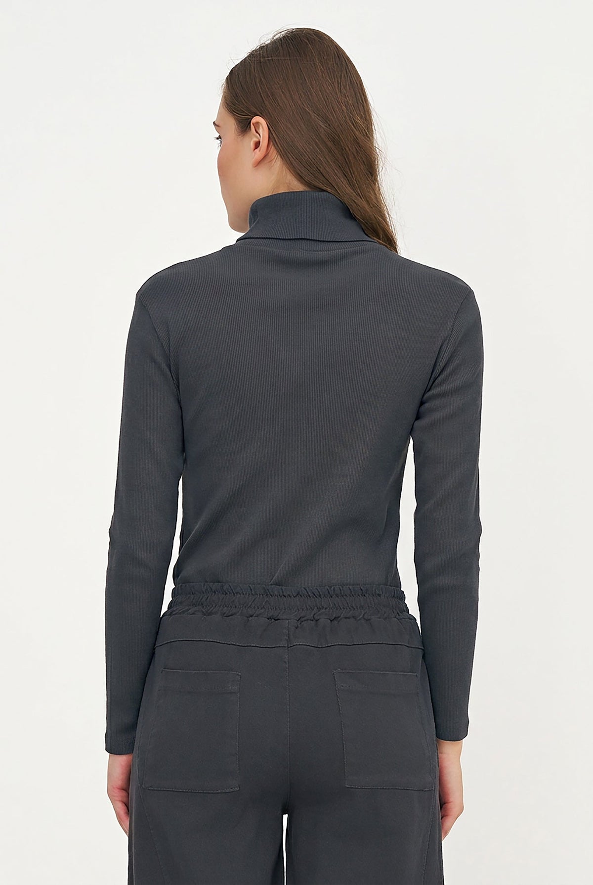 A woman shown from the back wearing a dark charcoal gray mock neck long-sleeve top and matching dark gray pants against a plain white studio background.