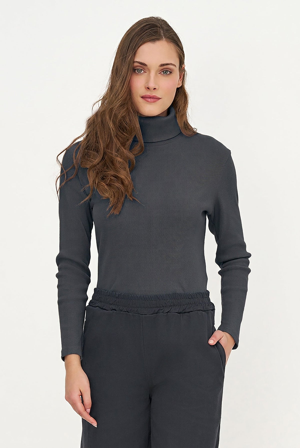 A woman modeling a dark gray long-sleeve mock neck top with matching dark gray trousers, photographed against a clean white studio background.