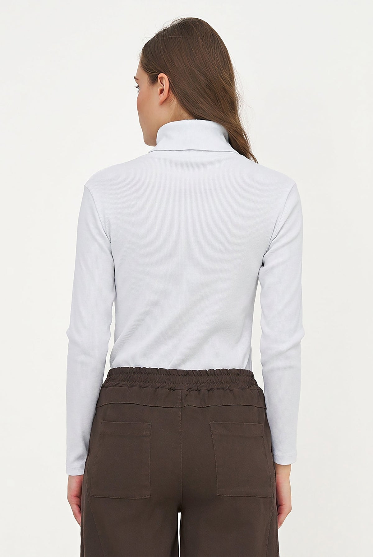 A woman shown from the back wearing a white mock neck long-sleeve top and dark brown pants against a plain white background.
