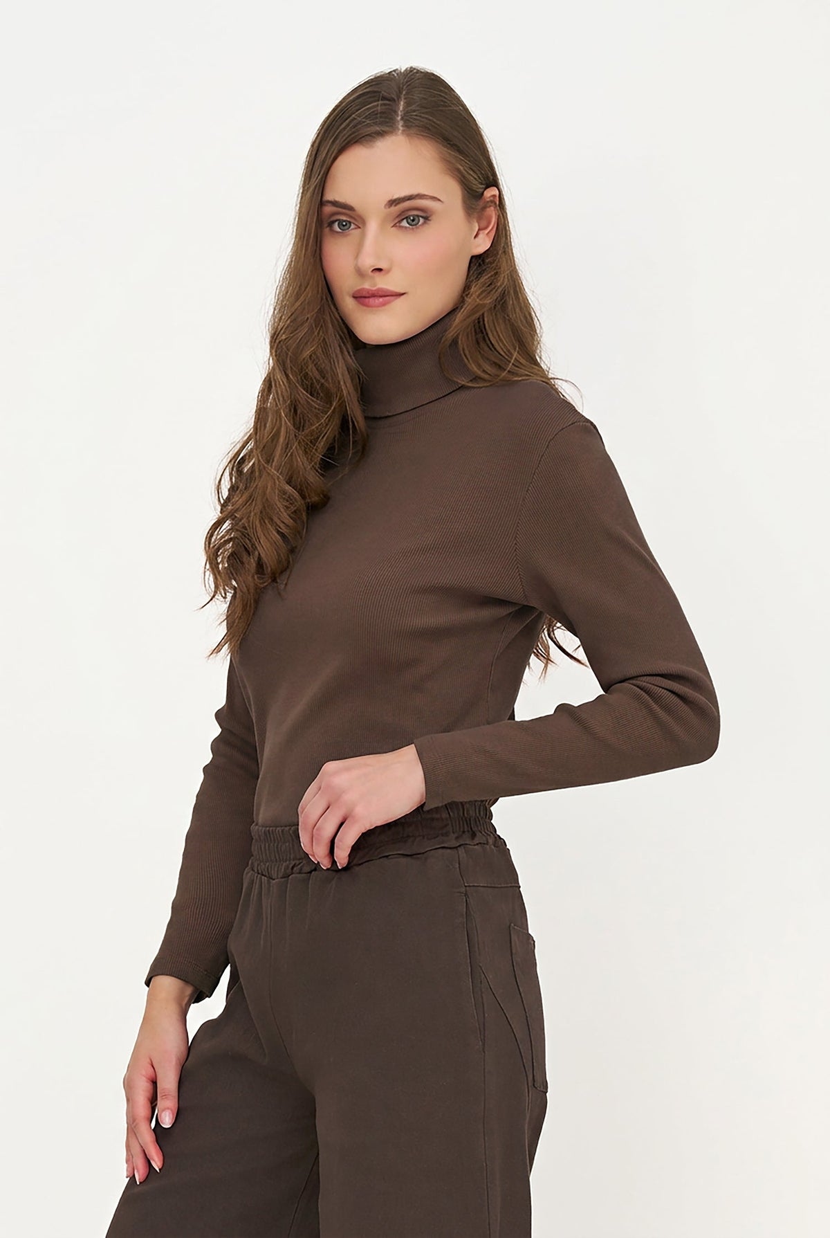A woman modeling a dark brown long-sleeve mock neck top and matching brown trousers against a plain white studio background.