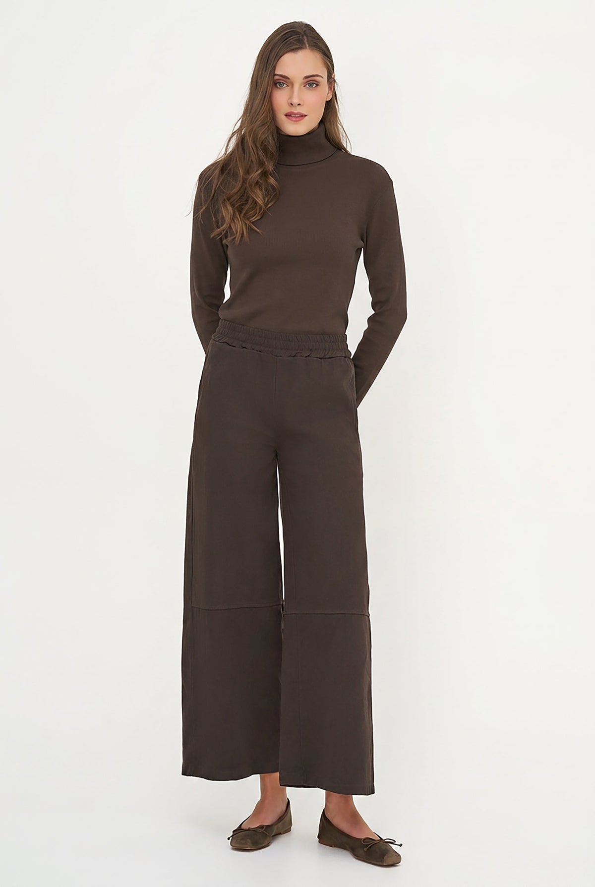 A woman modeling a dark brown long-sleeve mock neck top and matching brown trousers against a plain white studio background.