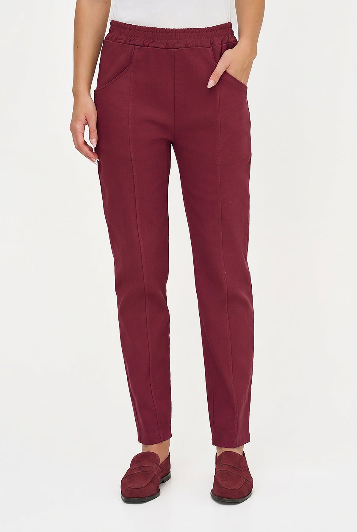 A person wearing slim-fit burgundy trousers with an elastic waistband, side pockets, and a straight tapered leg, paired with matching burgundy loafers against a plain white studio background.