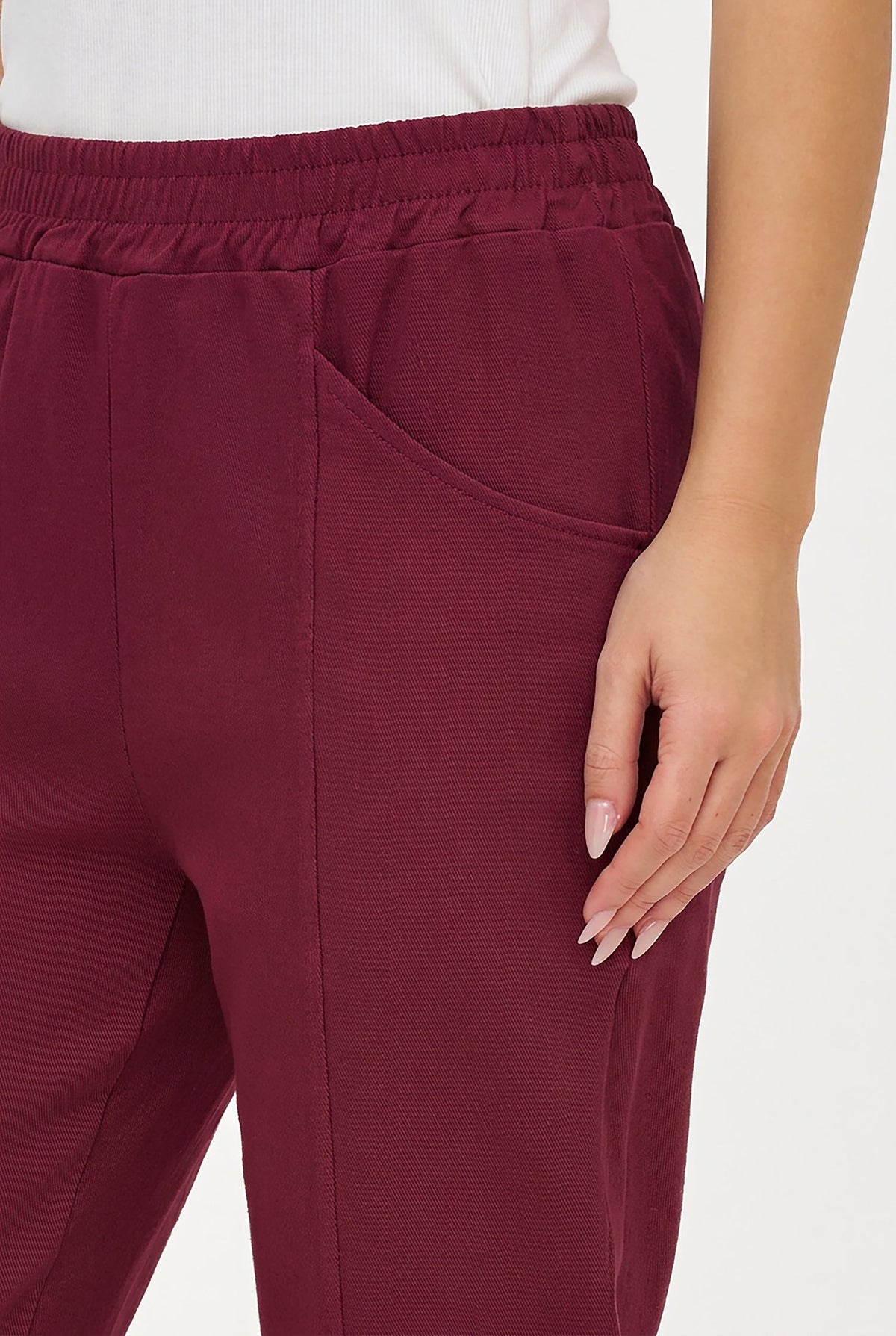 A close-up of a person wearing burgundy drawstring sweatpants with a side pocket, paired with a white top against a plain light background.