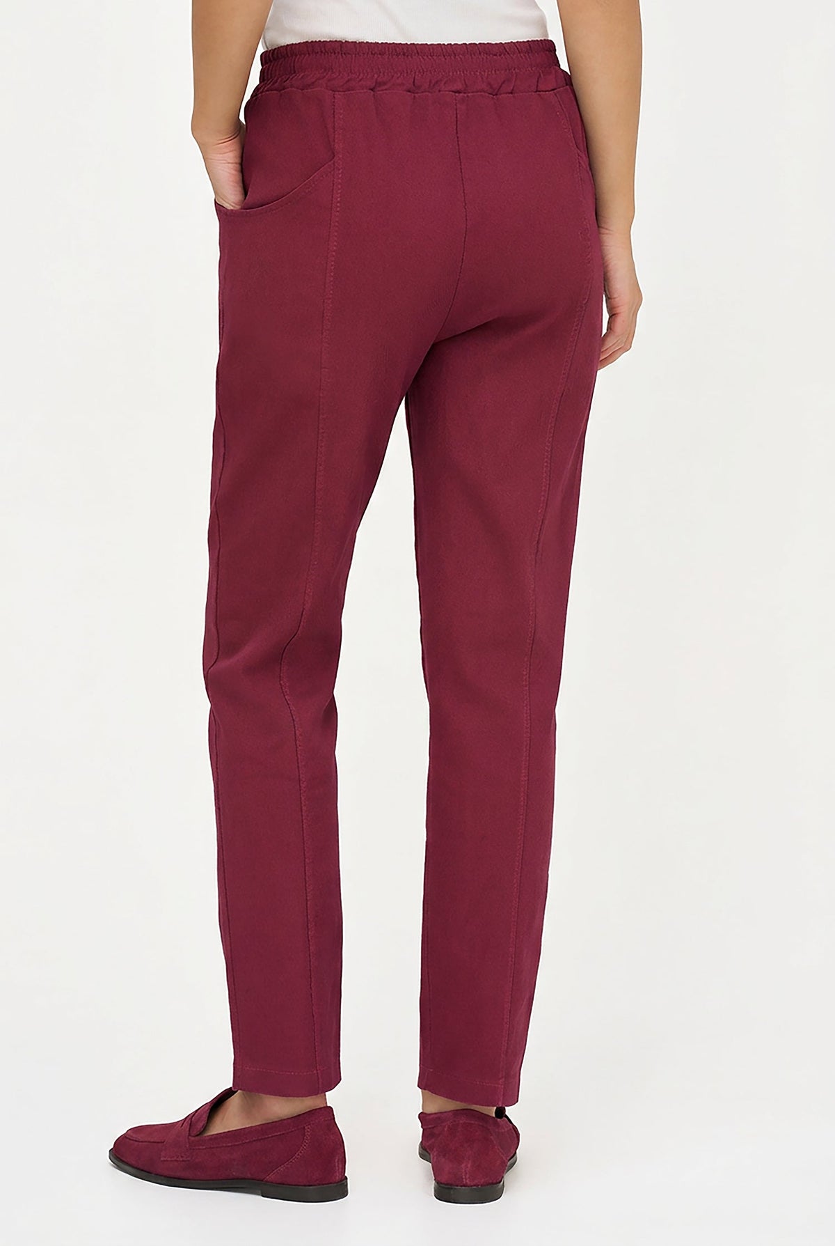 A person shown from the back wearing slim-fit burgundy trousers and matching burgundy flat shoes against a plain white studio background.