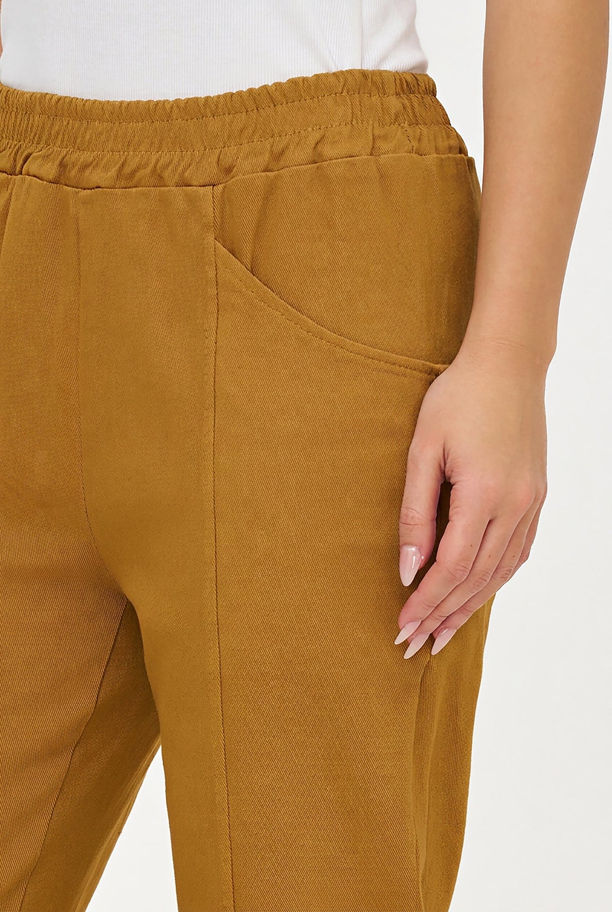 Close-up of a person wearing mustard yellow corduroy trousers with an elastic waistband and side pocket, paired with a white top against a light gray background.