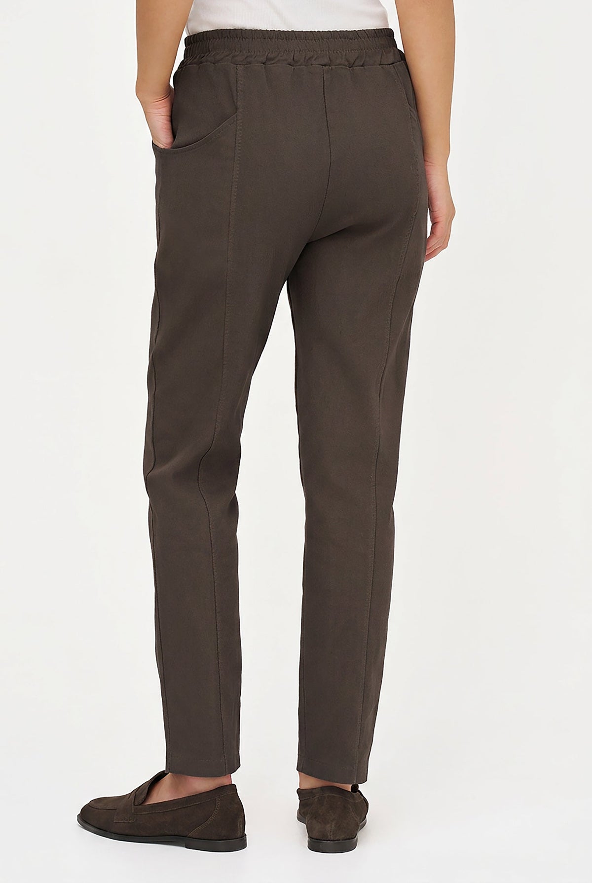 A person shown from the back wearing dark brown straight-leg trousers with side pockets and a braided waistband, paired with dark brown slip-on shoes against a plain white studio background.