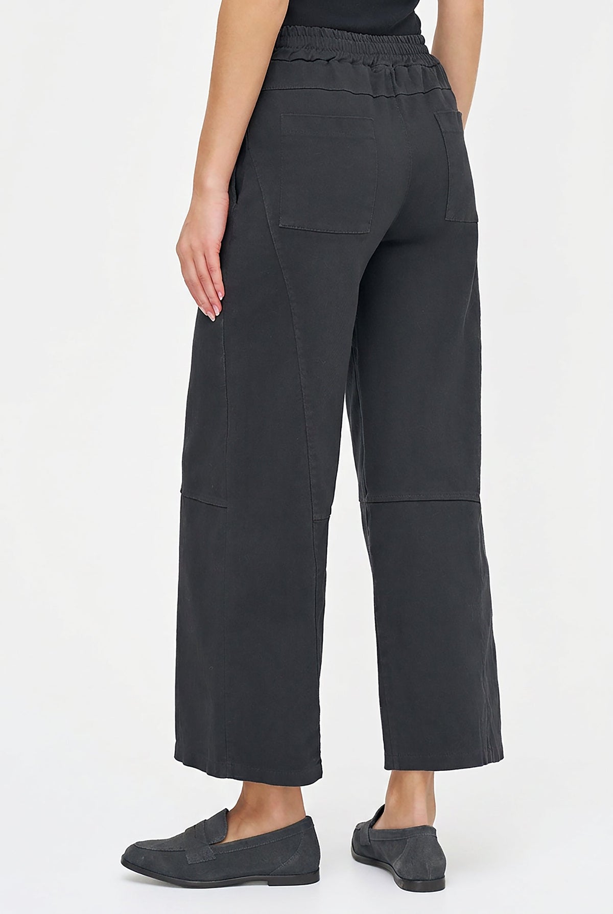 A model shown from the back wearing dark charcoal gray wide-leg cropped pants with an elastic waistband and side pockets, paired with dark gray slip-on shoes against a plain white studio background.