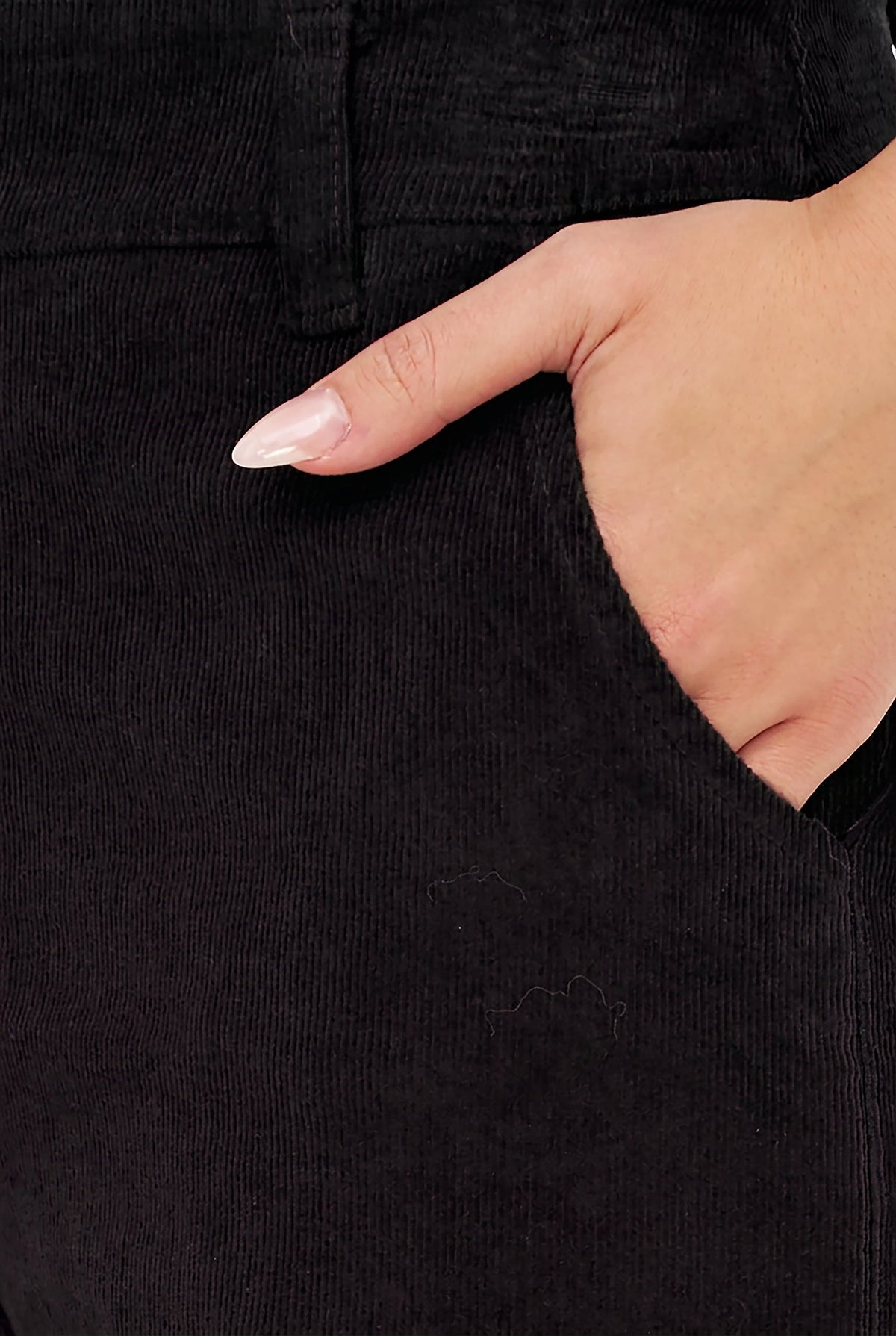 Close-up of a person wearing black corduroy trousers, showing the texture of the fabric and a hand reaching into the side pocket.