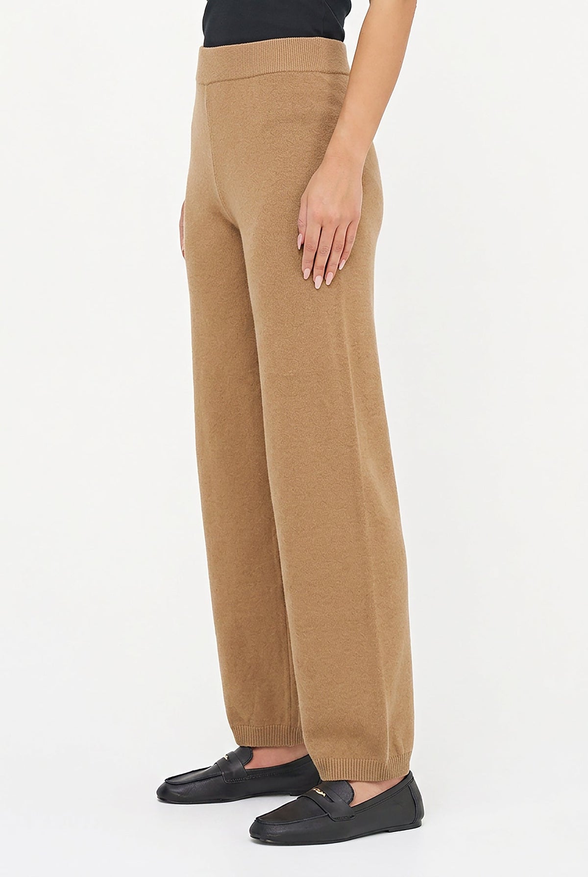 A model wearing a pair of wide-leg, straight-fit trousers in camel brown, paired with black loafers, shown from the waist down against a plain white studio background.