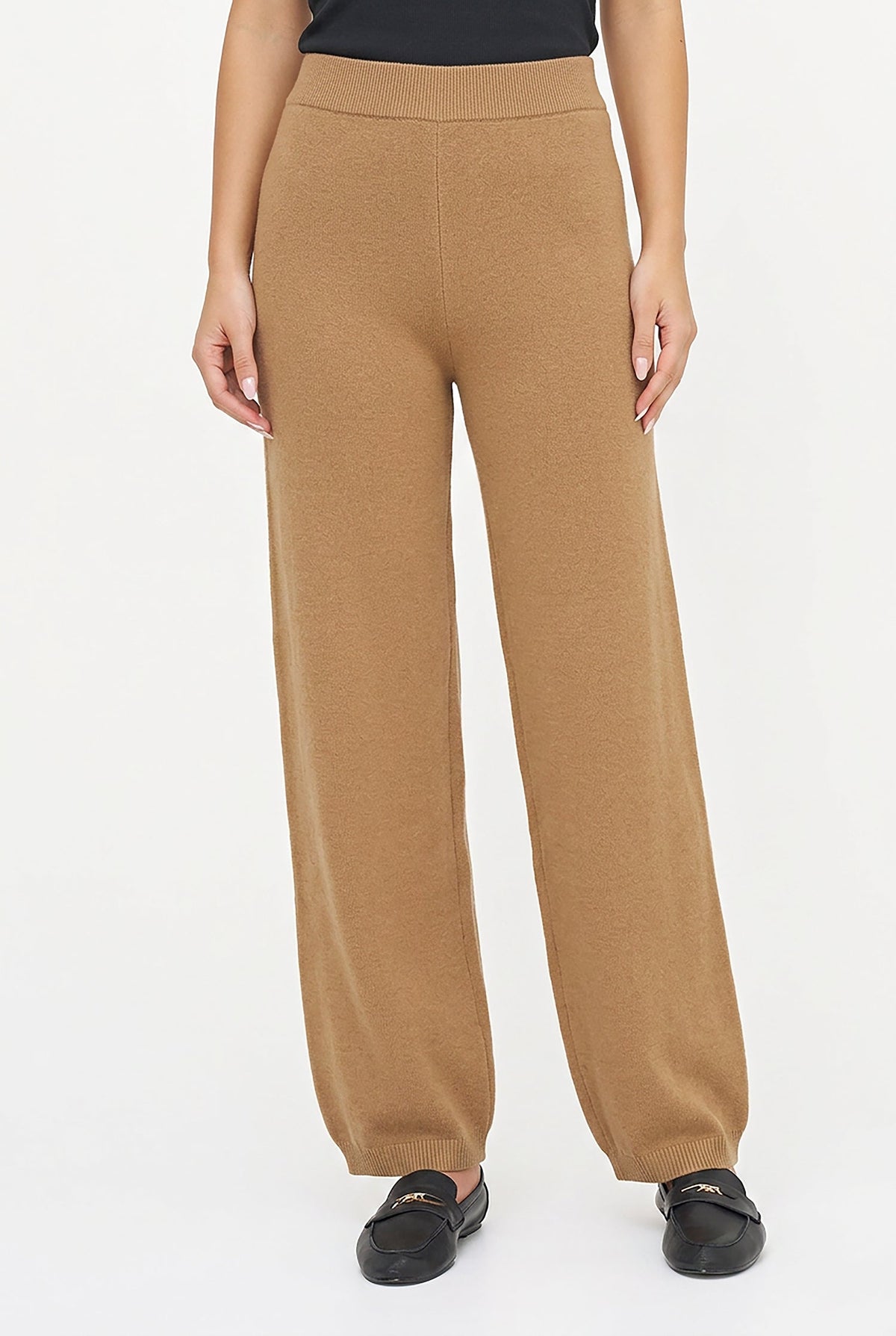 A model wearing a pair of wide-leg, high-waisted knit pants in camel brown, paired with black loafers, against a plain white studio background.