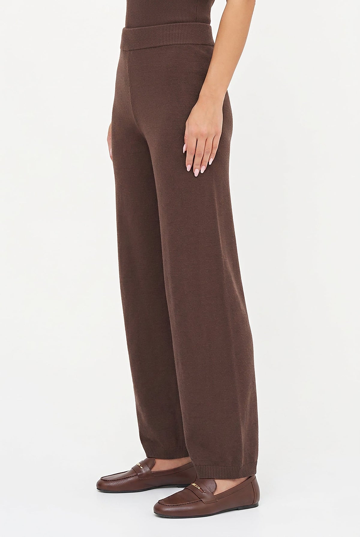 A model wearing high-waisted, wide-leg brown knit pants paired with matching brown leather loafers, shown from the waist down against a plain white studio background.
