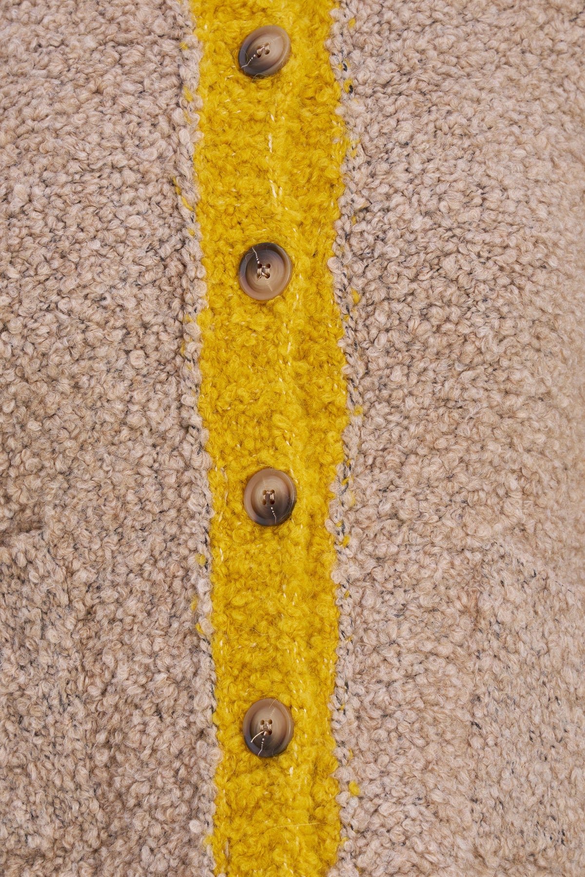 Close-up of a beige textured knit garment with a bright yellow vertical stripe running down the center and five brown buttons along the front.