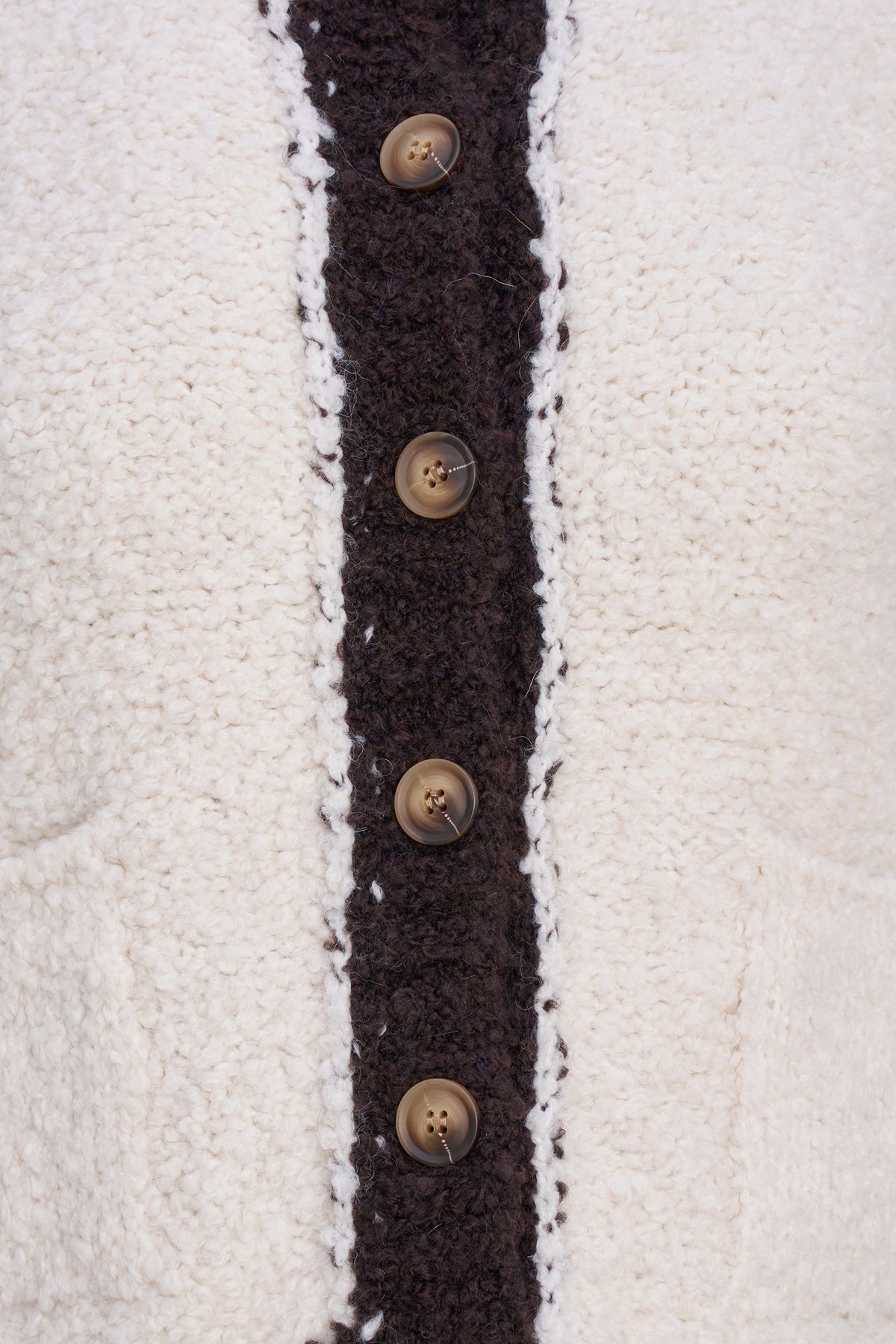 Close-up of a textured cream sherpa cardigan featuring a dark brown fuzzy trim down the center with four brown buttons.