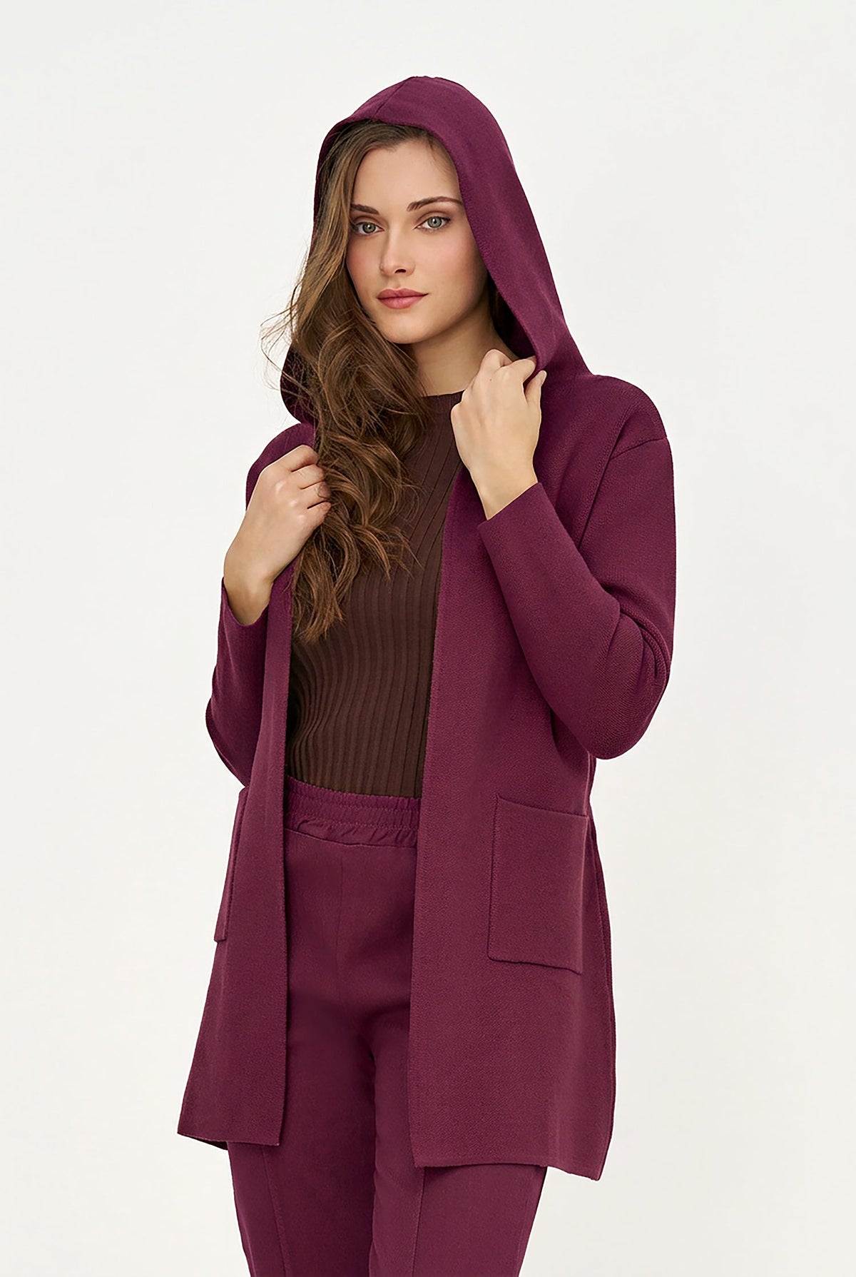 A woman modeling a matching deep plum purple lounge set, featuring a hooded cardigan, a ribbed brown top, and matching pants, against a plain white studio background.