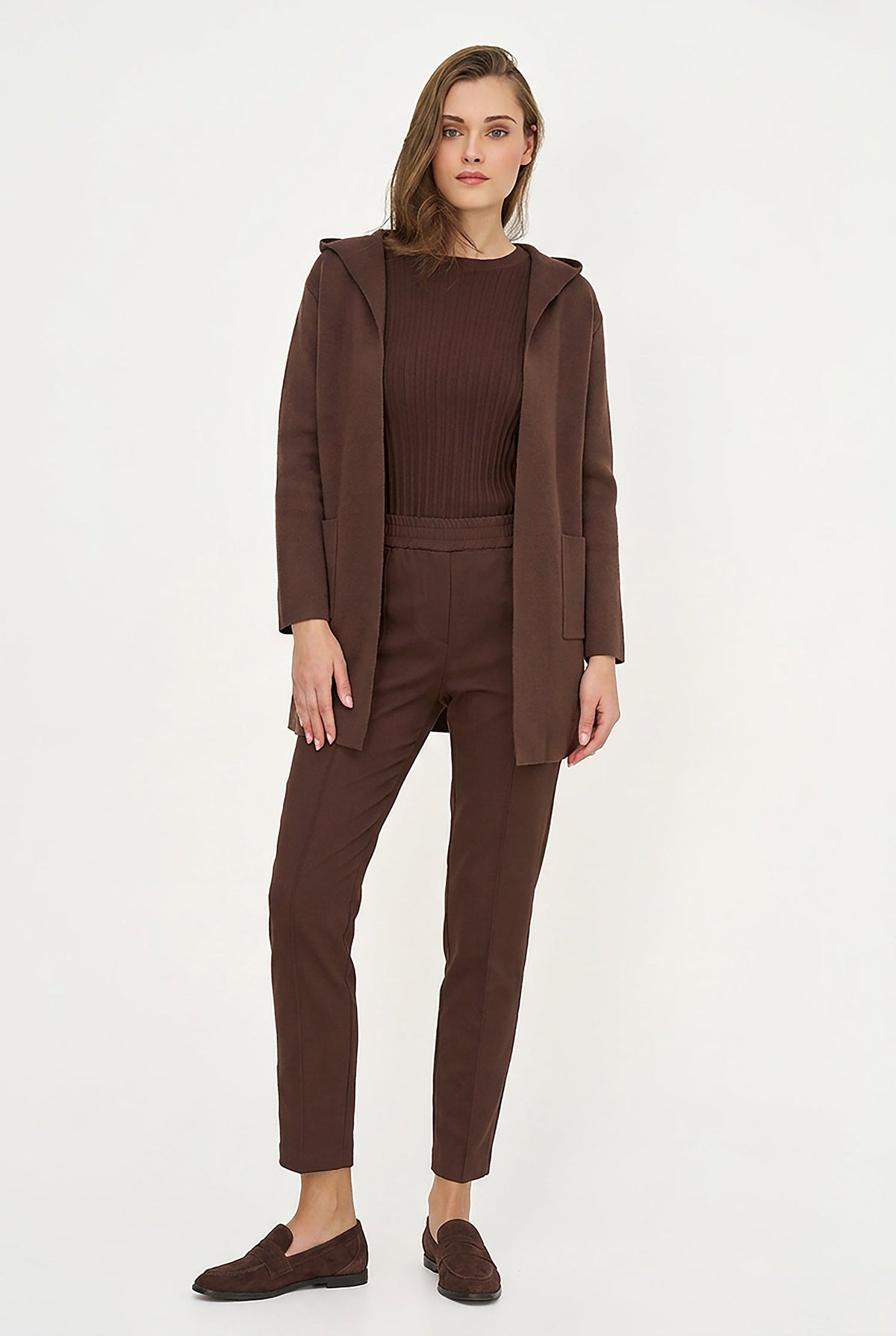 A woman modeling a matching dark brown outfit consisting of a hooded jacket, ribbed knit top, slim-fit trousers, and loafers, set against a plain white studio background.