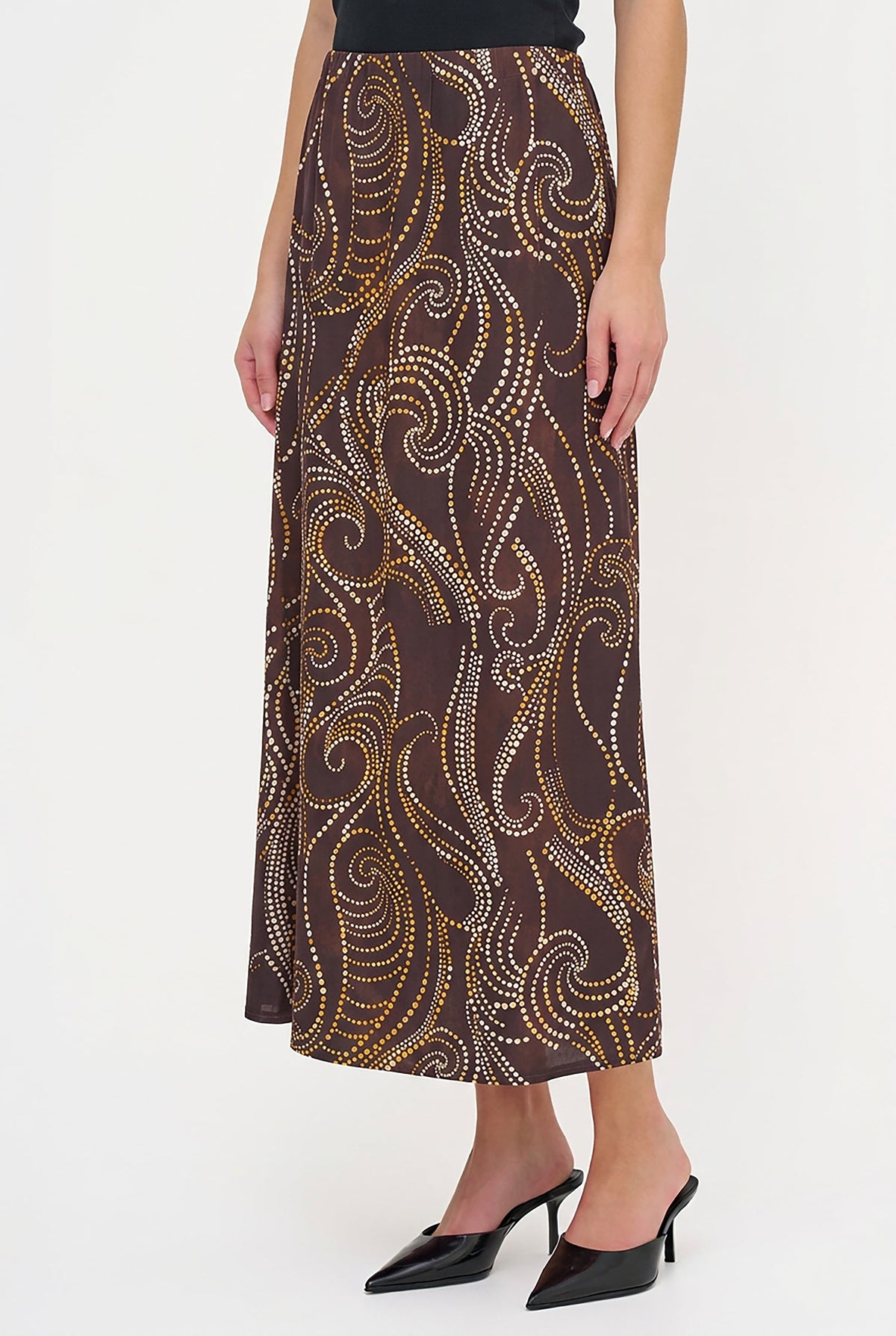 A model wearing a brown midi skirt with a gold and white abstract swirl pattern, paired with black pointed-toe mule heels against a plain white studio background.