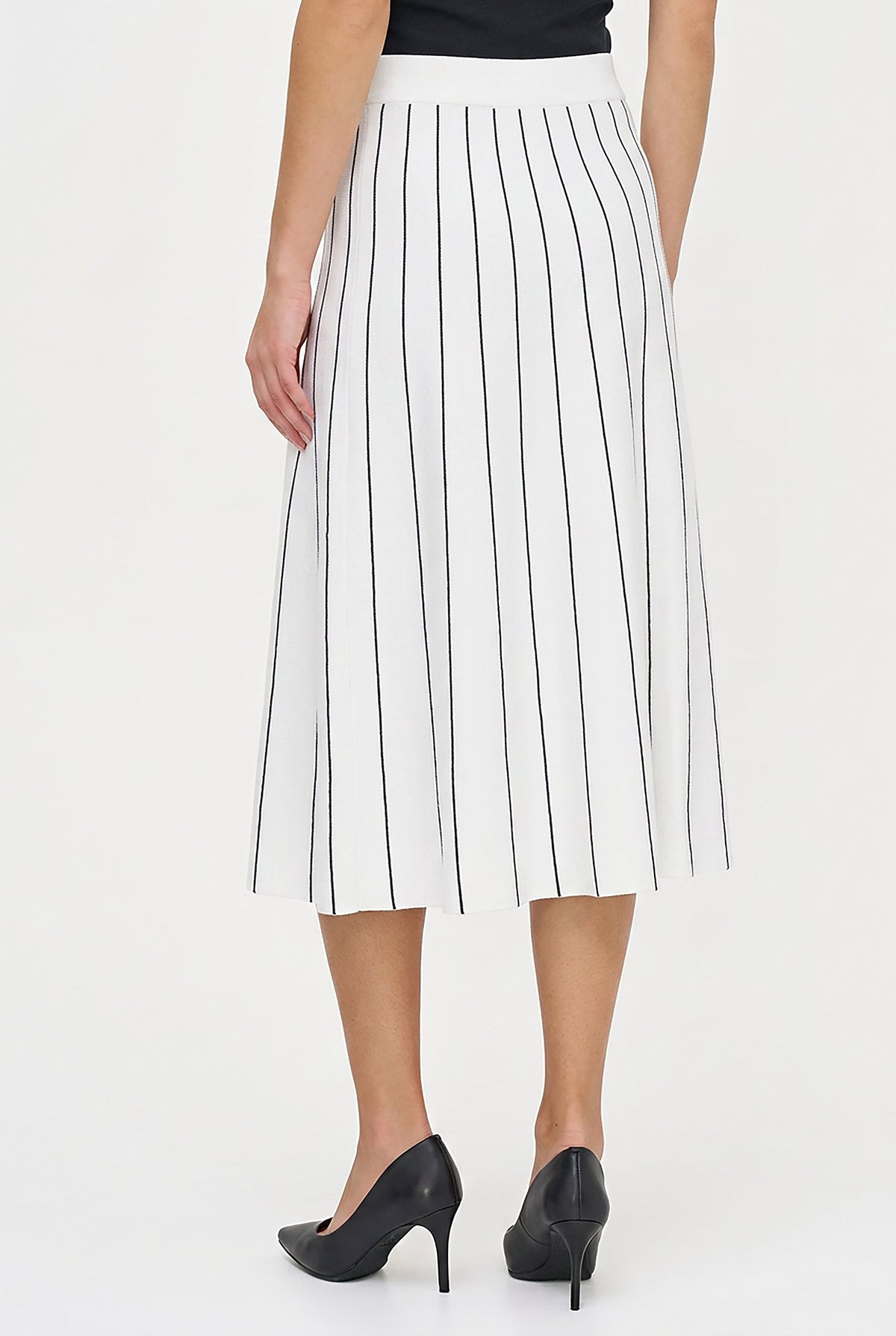 A model from the back wearing a white midi skirt with thin black vertical pinstripes, paired with black pointed-toe heels against a plain white studio background.