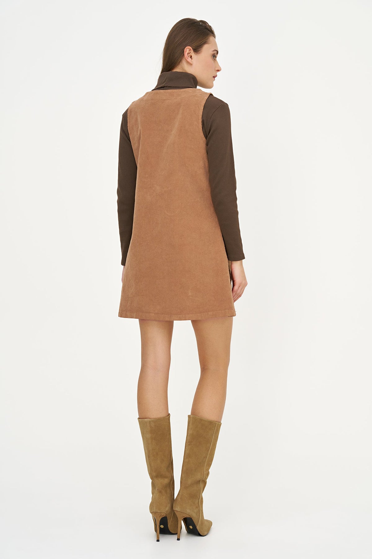 A model shown from the back wearing a brown suede sleeveless vest over a dark brown long-sleeve top, paired with tan suede knee-high boots, against a plain white studio background.