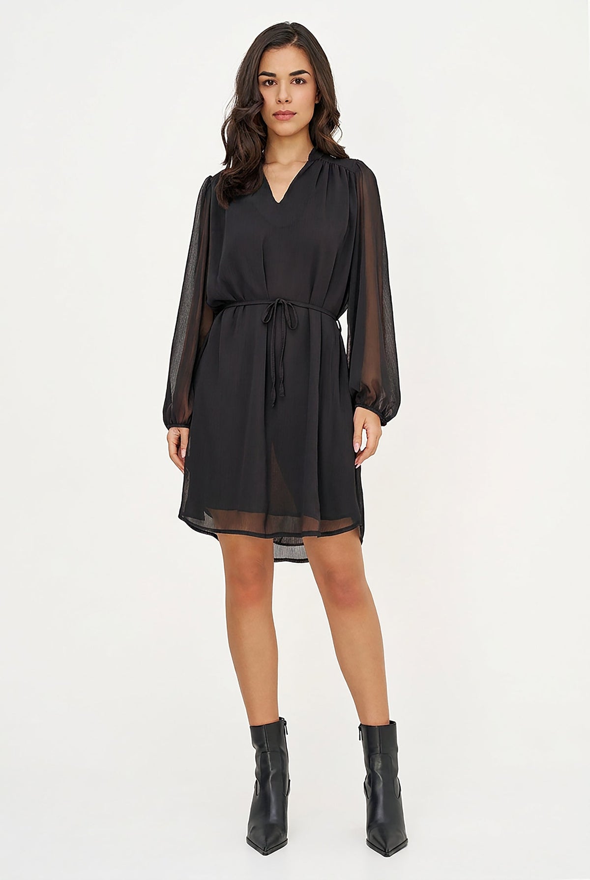 A woman modeling a black long-sleeve mini dress with sheer mesh sleeves and a matching fabric tie belt, paired with black ankle boots, against a plain white studio background.