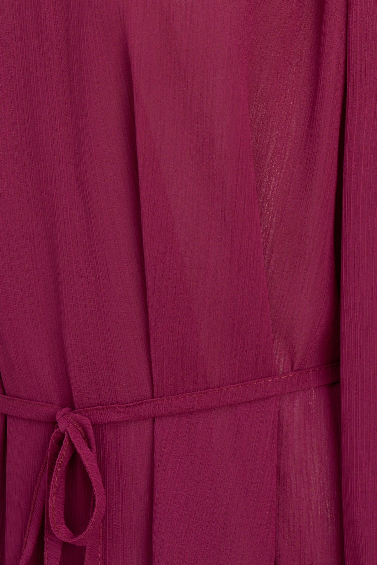 A close-up of a magenta pink crinkled fabric garment with a matching tie belt at the waist.