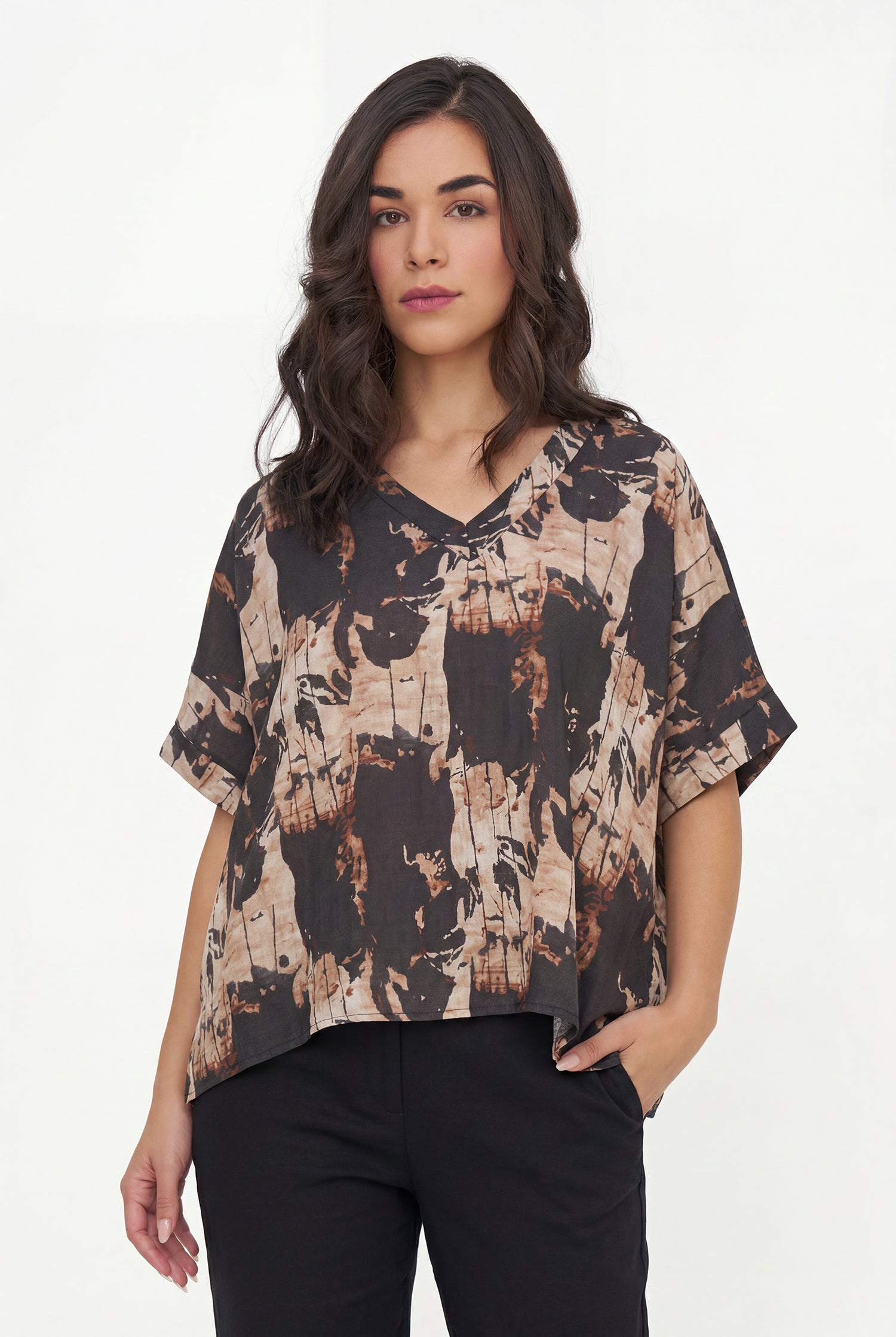 Woman wearing a patterned top and black pants on a white background