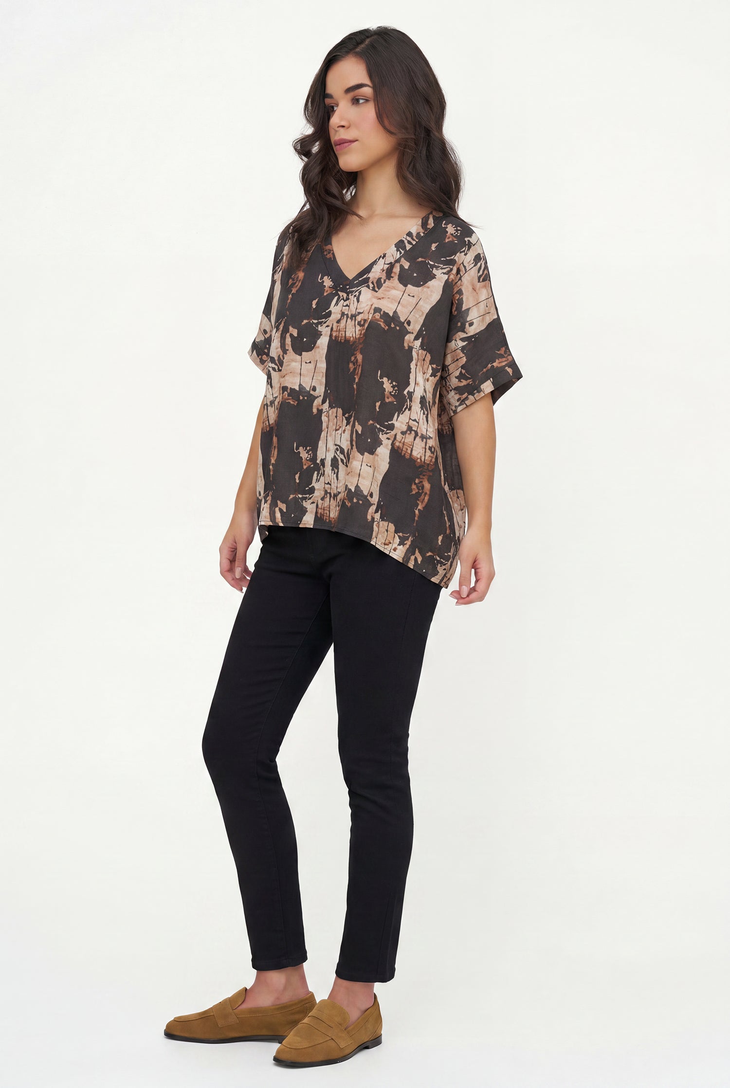 Woman wearing a patterned top and black pants on a white background