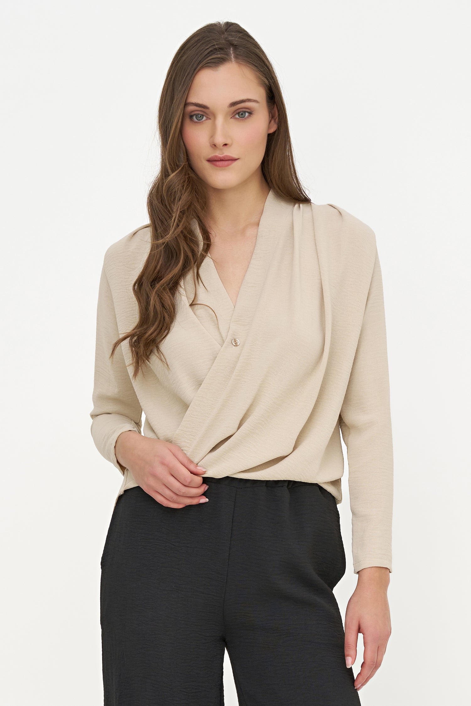 Woman wearing a beige wrap tunic top and black pants on a white background