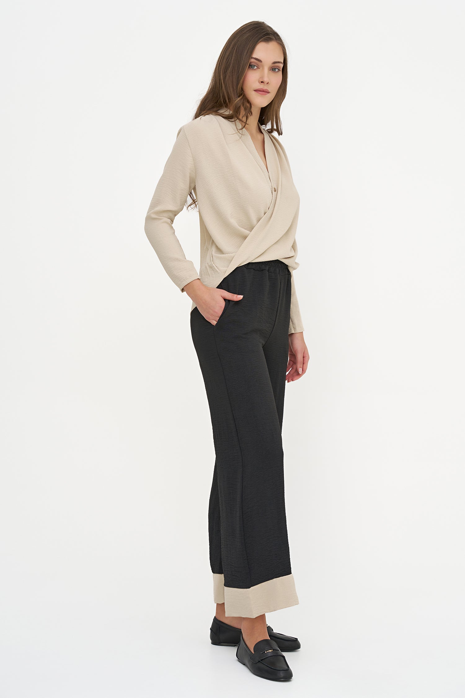 Woman wearing a beige blouse and black pants on a white background