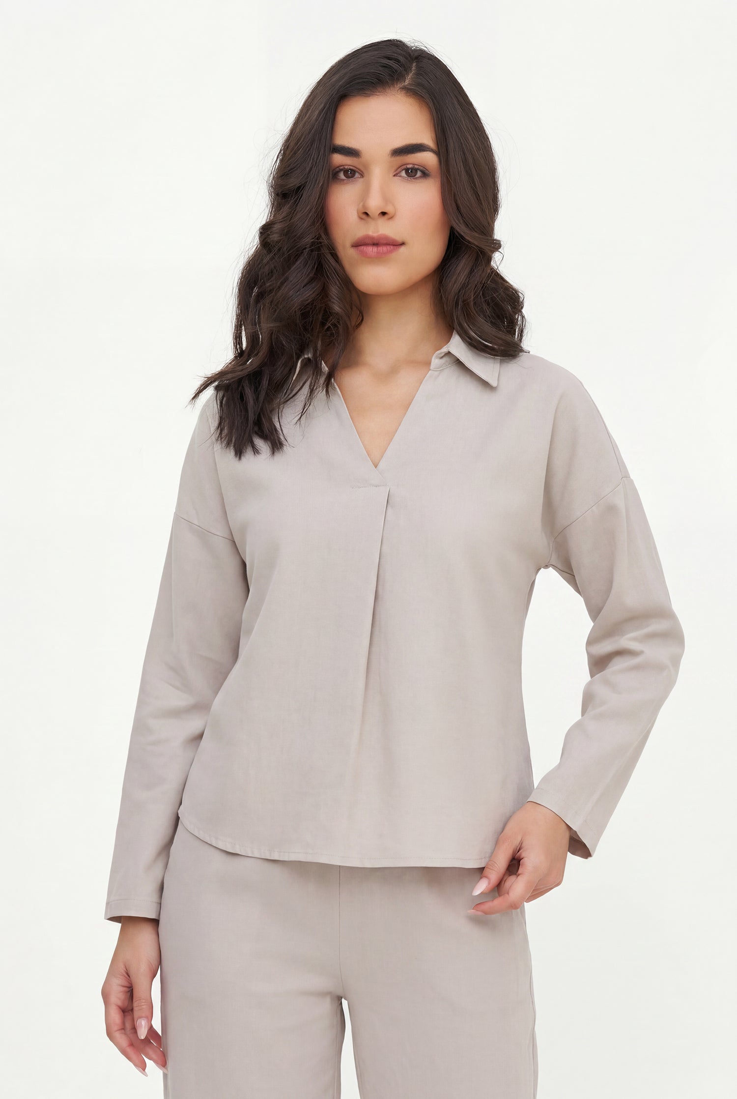 Woman wearing a beige long-sleeve shirt and pants on a white background