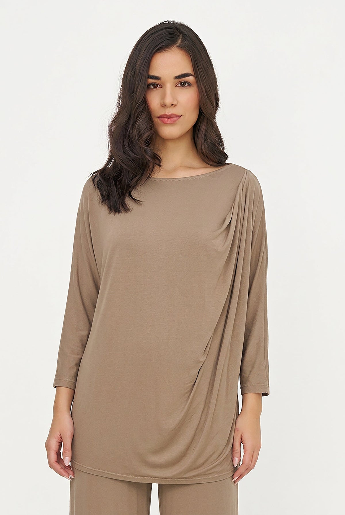 A woman modeling a taupe brown long-sleeve draped tunic top with matching pants against a plain white studio background.
