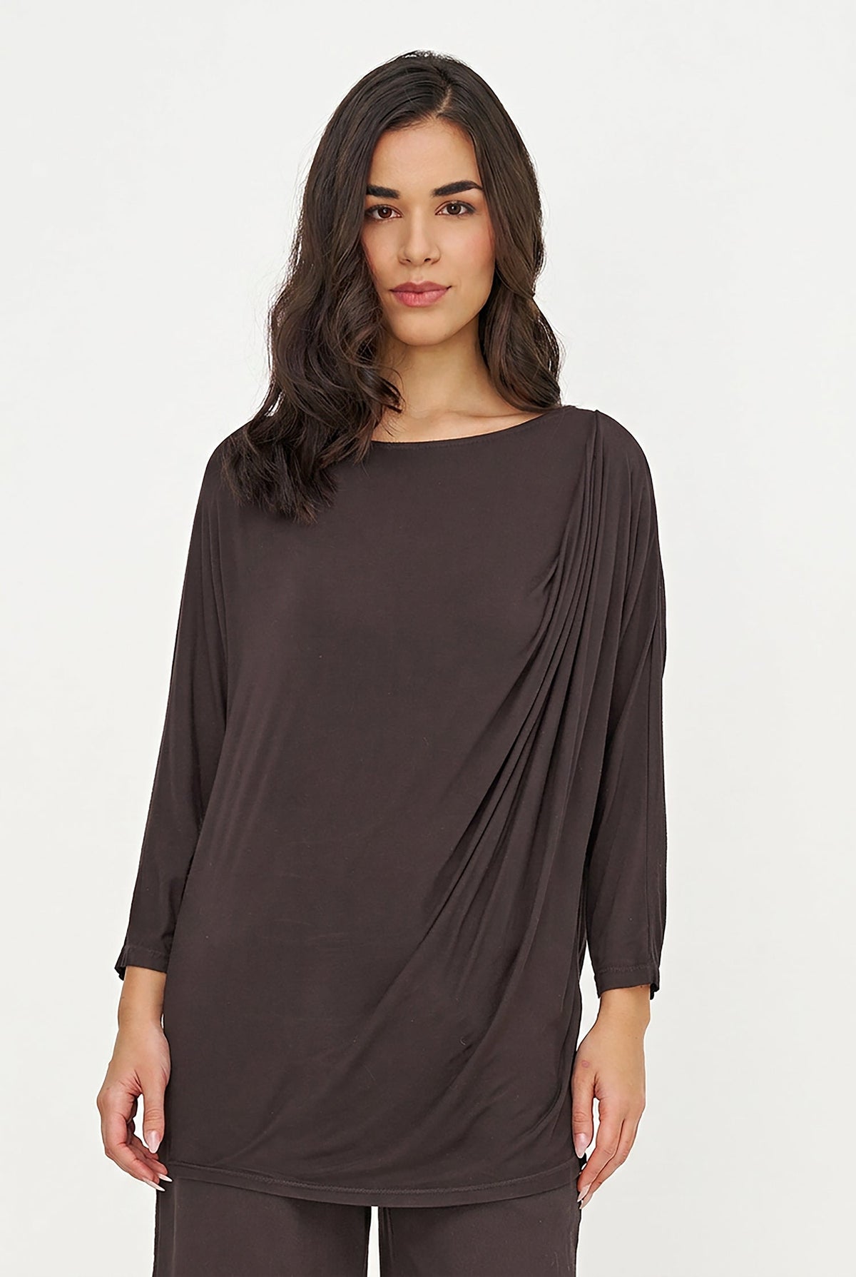 A woman modeling a black long-sleeve draped tunic top against a plain light gray studio background.
