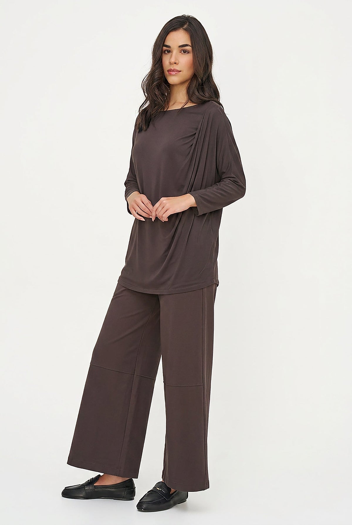 A woman modeling a black draped long-sleeve top and matching wide-leg pants against a plain white studio background.
