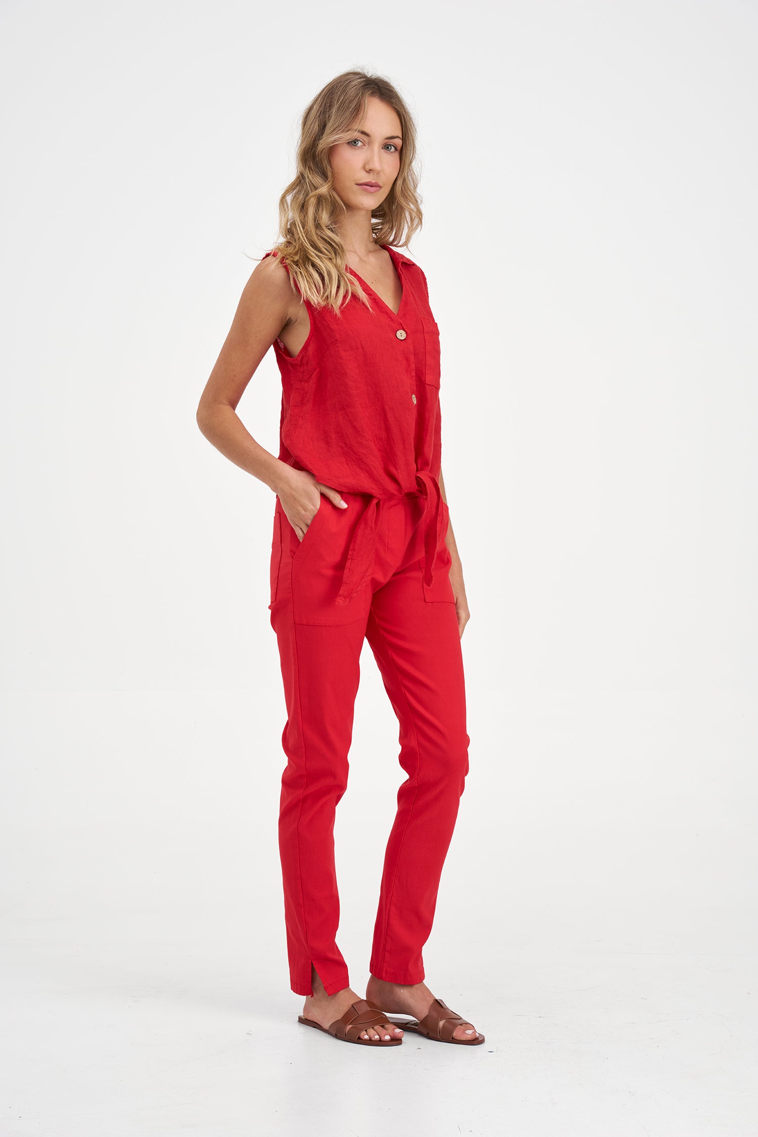 Woman wearing a red sleeveless button-up top with a tie waist and pants on a white background