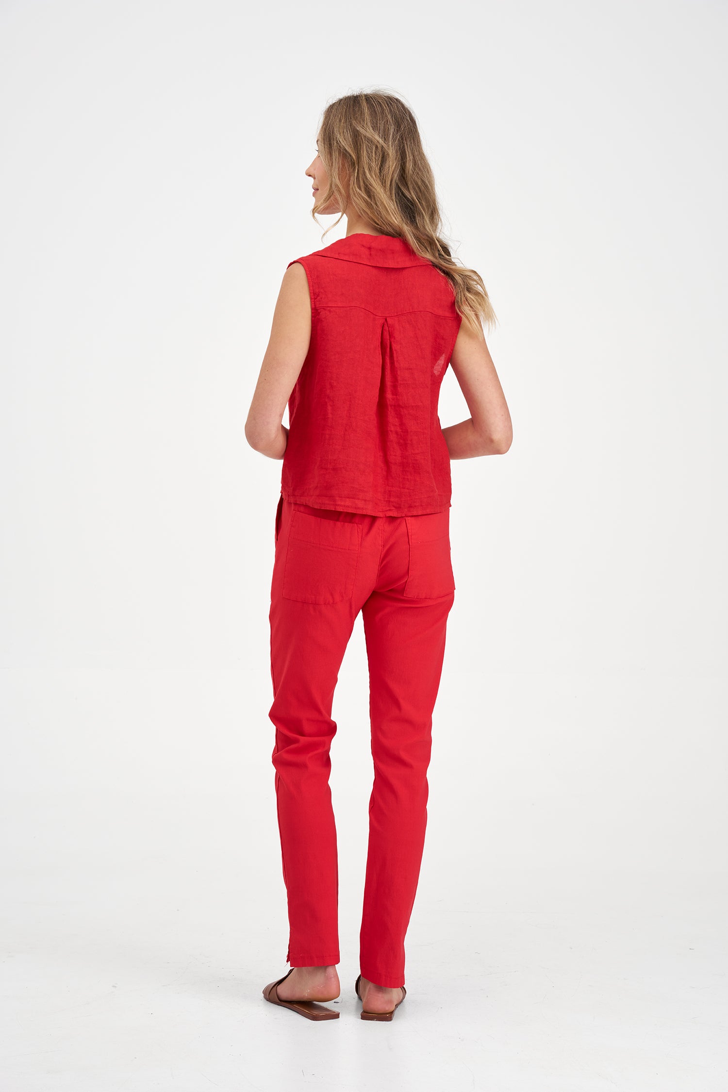 Woman's back wearing a red sleeveless button-up top with a tie waist and pants on a white background