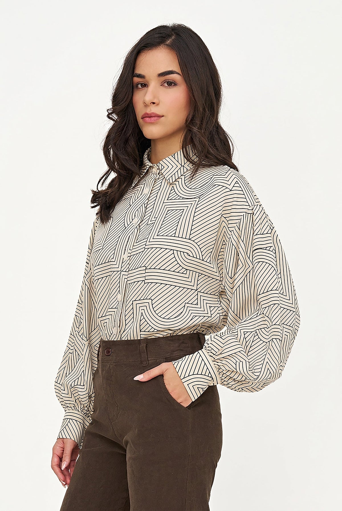 A woman wearing a beige and black geometric patterned long-sleeve blouse with black pants, photographed against a plain light background.