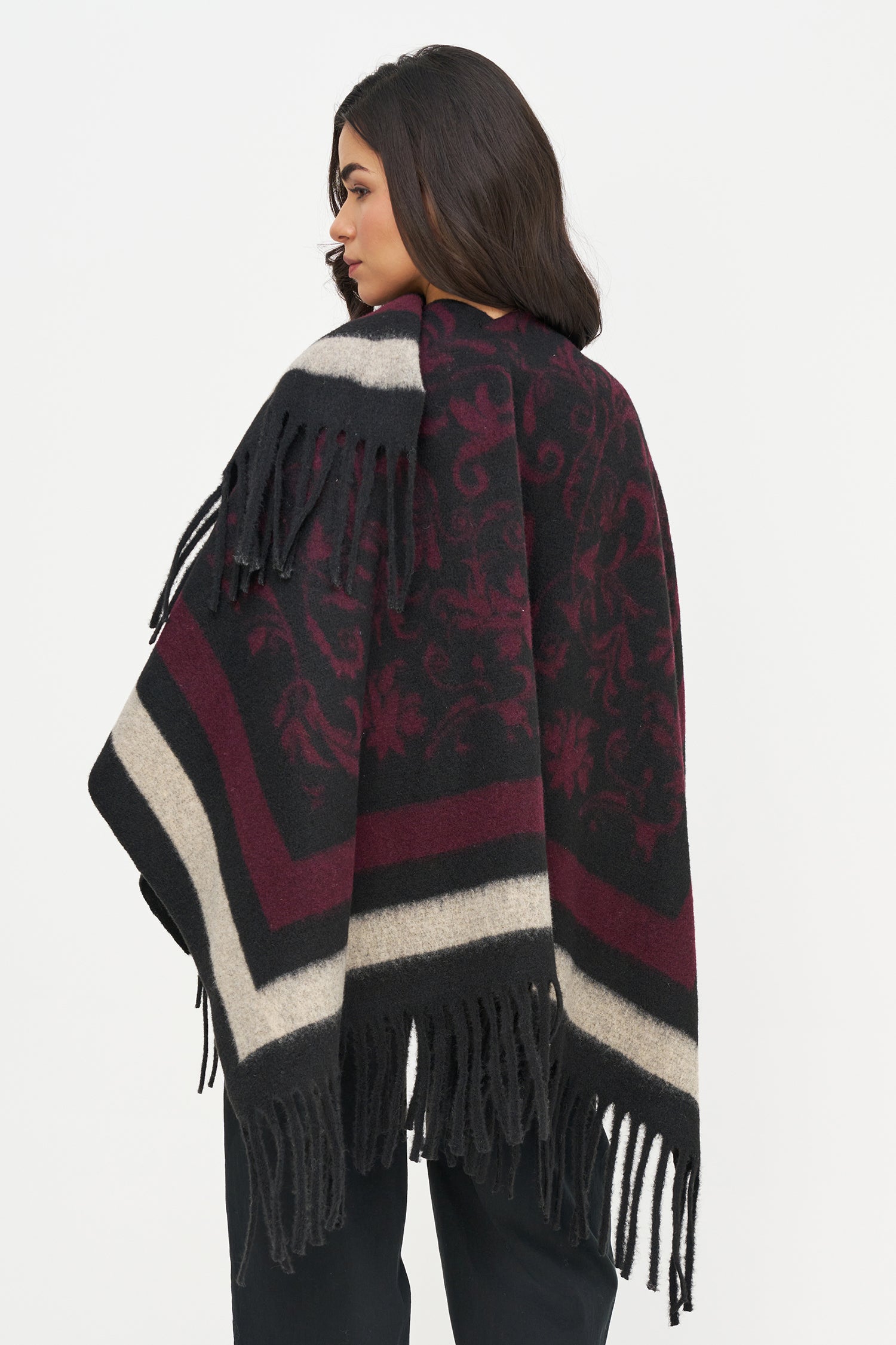 Woman wearing a patterned poncho with fringes on a white background