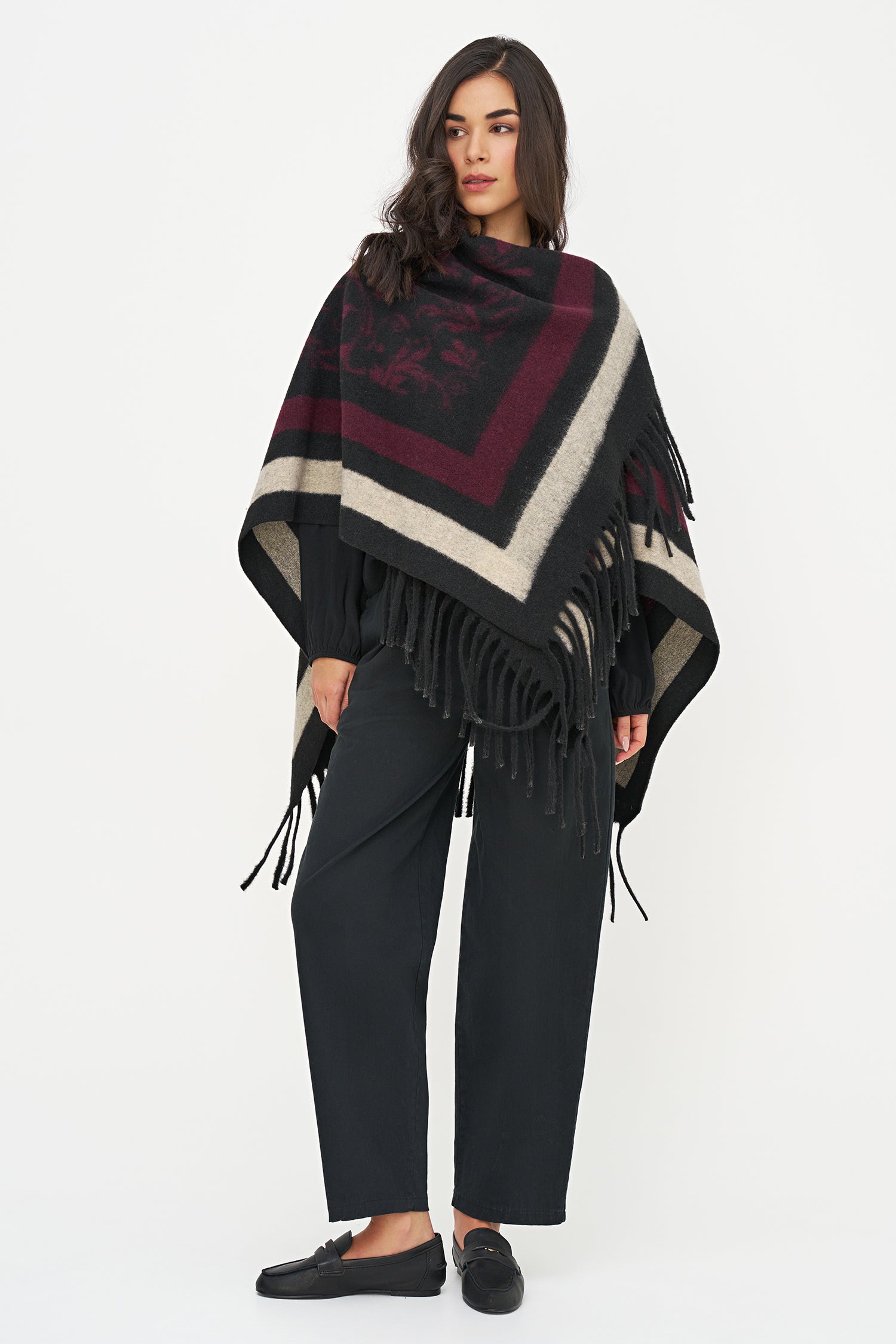 Woman wearing a patterned poncho with fringes on a white background