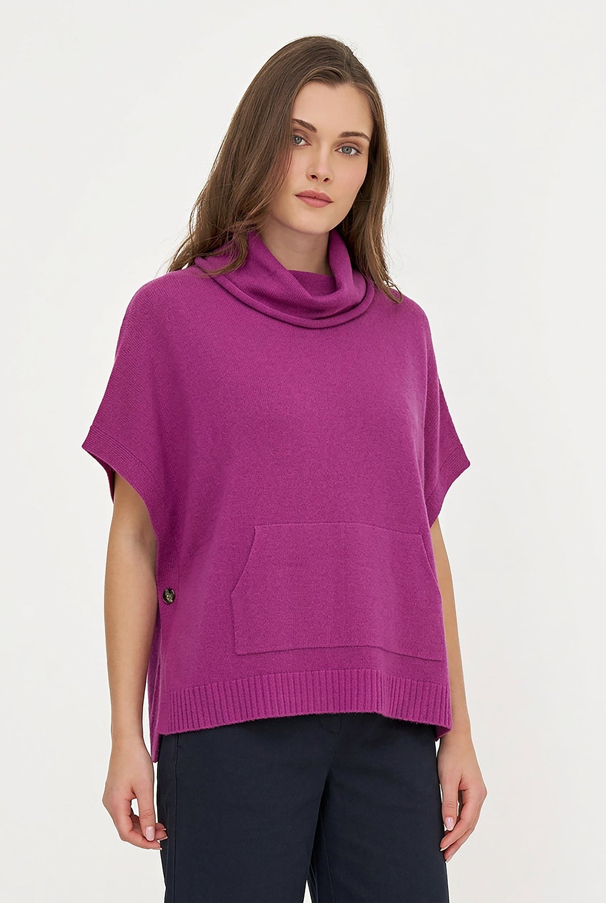 A woman shown from the back wearing a bright magenta knit poncho-style top with a folded cowl neck and short sleeves, paired with black pants, against a plain light background.