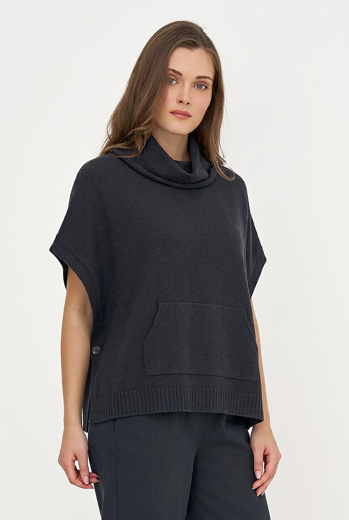 A woman shown from the back wearing a dark charcoal gray knit poncho sweater with a cowl neck and short wide sleeves, paired with dark pants, against a plain white studio background.