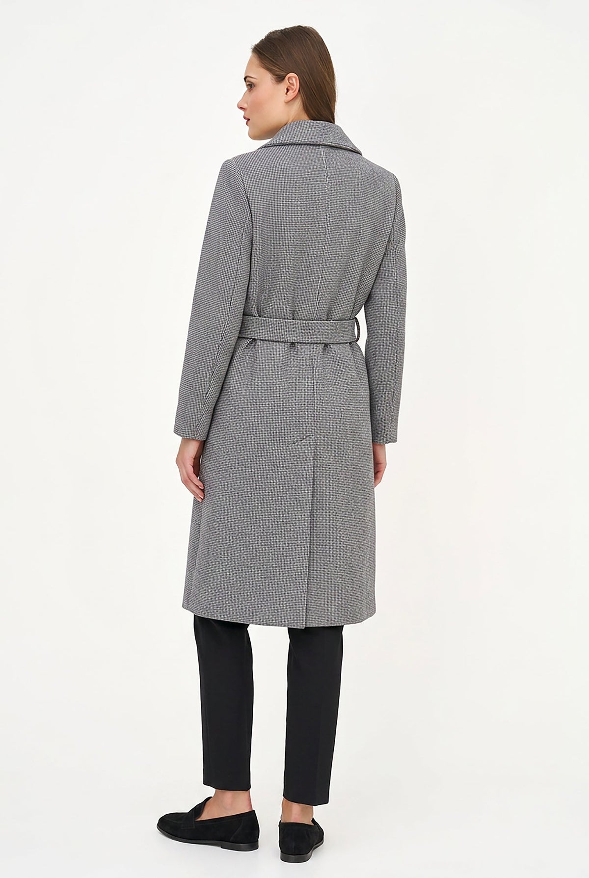 A woman shown from the back wearing a mid-length gray belted coat over black pants and black flats, photographed against a plain white studio background.