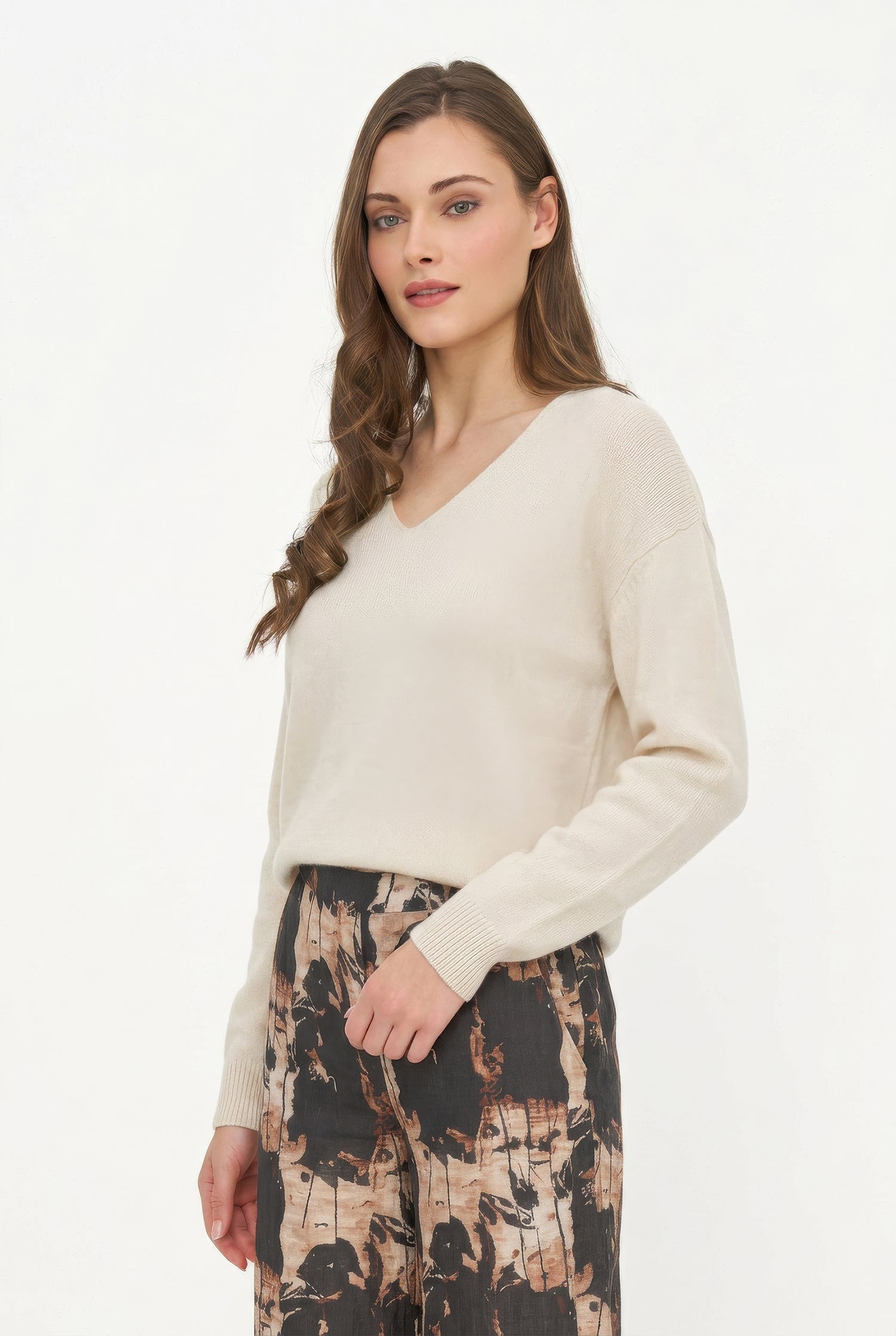 Woman wearing a cream sweater and patterned pants on a white background