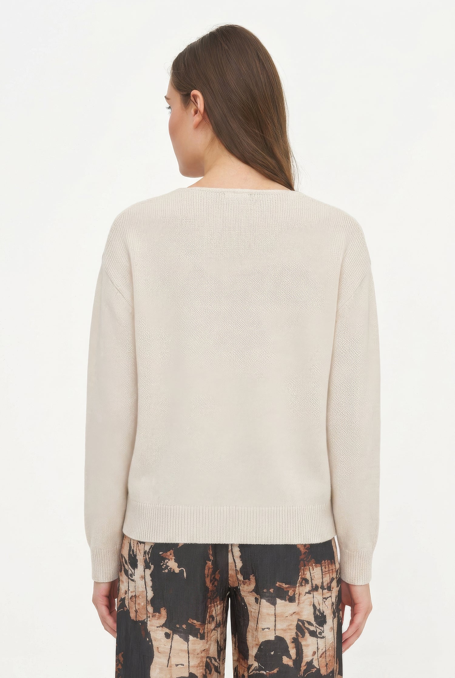 Woman wearing a beige sweater with patterned pants on a white background