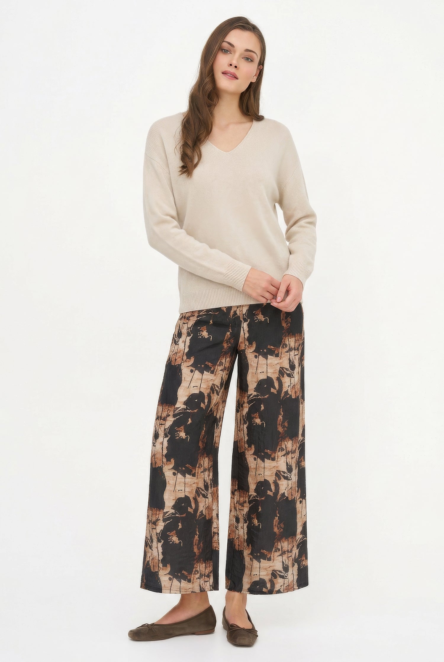 Woman wearing a beige sweater and patterned pants on a white background