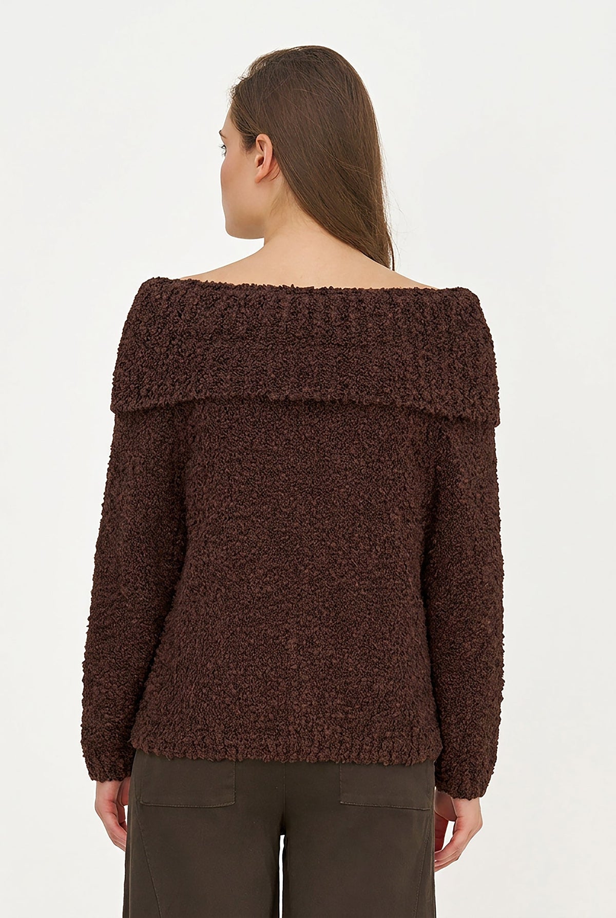 A woman shown from the back wearing a dark brown textured off-the-shoulder sweater and dark brown pants against a plain white studio background.