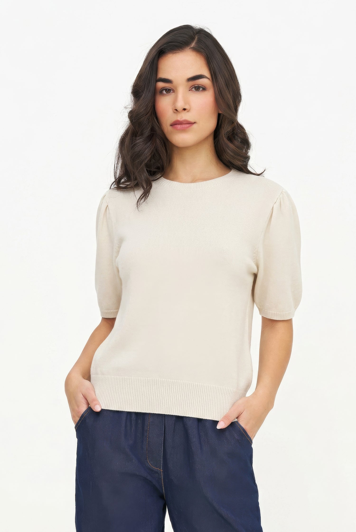 Woman wearing a beige sweater and navy pants on a white background