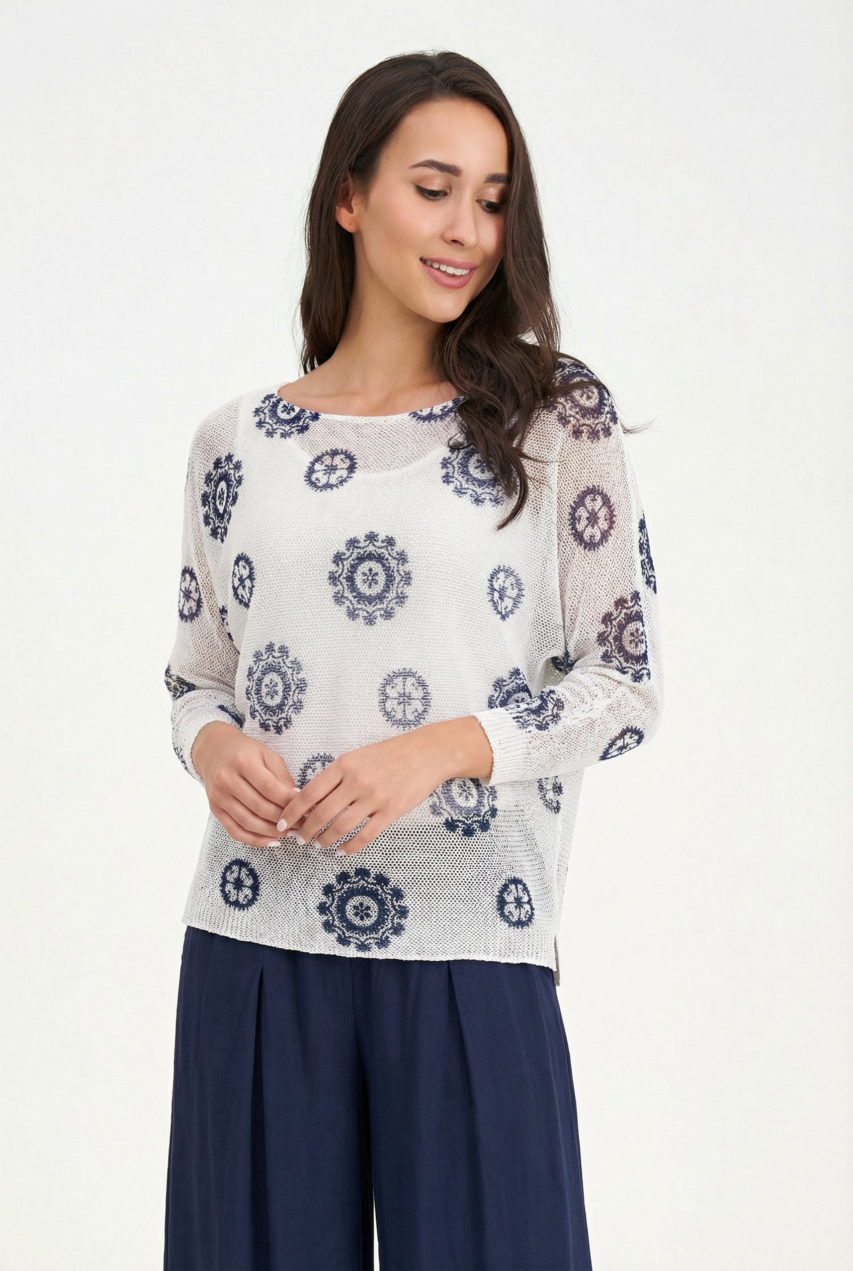 Woman wearing a white sweater with blue floral patterns on a white background