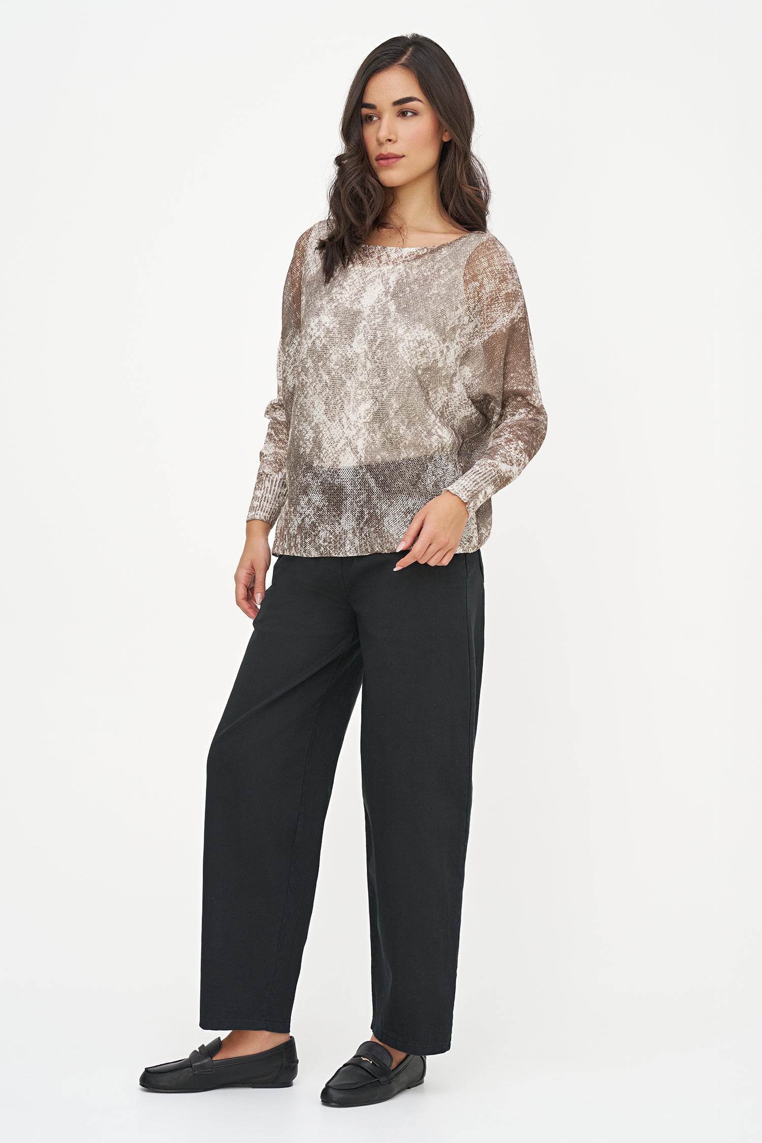 Woman wearing a patterned top and black pants on a white background